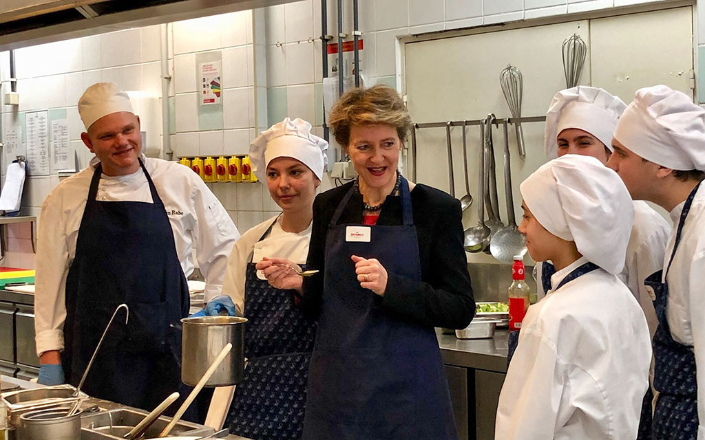 Bundesrätin Simonetta Sommaruga steht in einer Küche zusammen mit angehenden Köchinnen und Köchen, die in einem Projekt eine Berufslehre nach Schweizer Vorbild absolvieren.